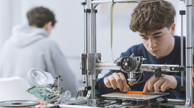 A young man checking his test print on a 3D printer bed