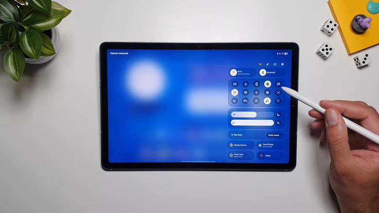 A hand holding an S Pen pointing at the Quick Settings on a Samsung Galaxy tablet