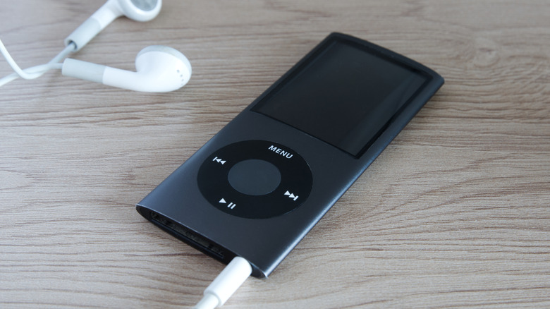 A black 4th-generation iPod Nano on a table with Apple earbuds plugged in