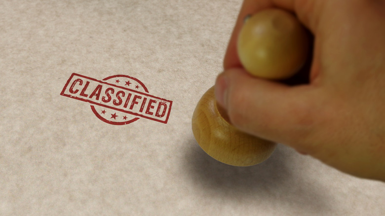 A hand has just stamped "classified" onto a document.