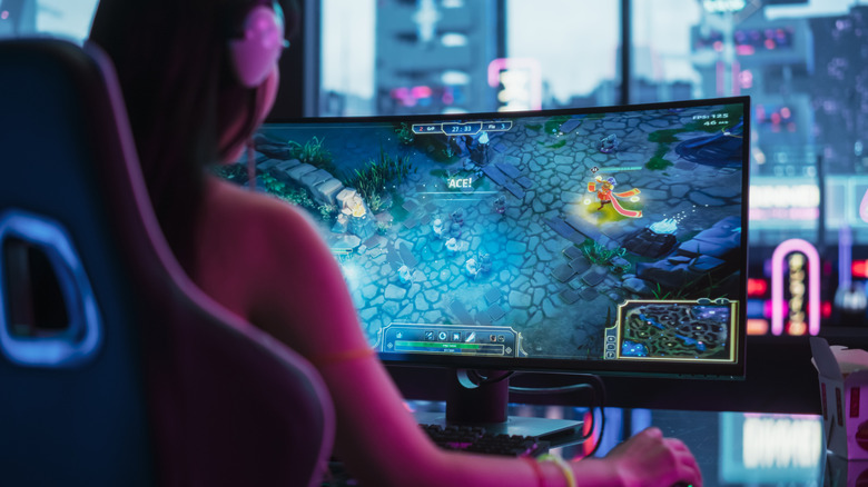 Woman playing MOBA game on curved monitor with headset
