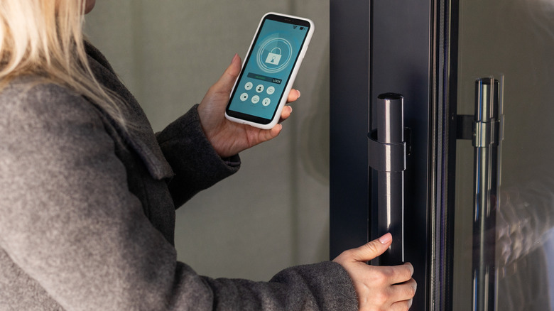 Woman holding a smartphone with a lock symbol onscreen while opening a door