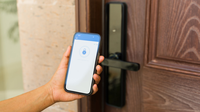 Person holding a smartphone with a lock symbol onscreen up to a door lock