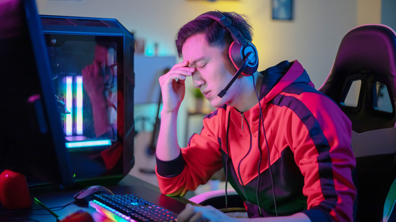A person gaming on a PC looking frustrated or tired
