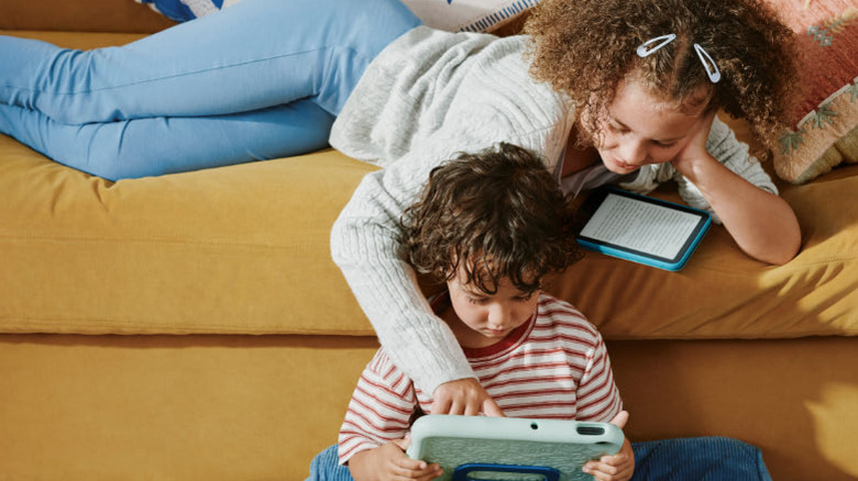 woman with curly hair reading a kindle while her son plays on an Amazon tablet with Amazon Kids+