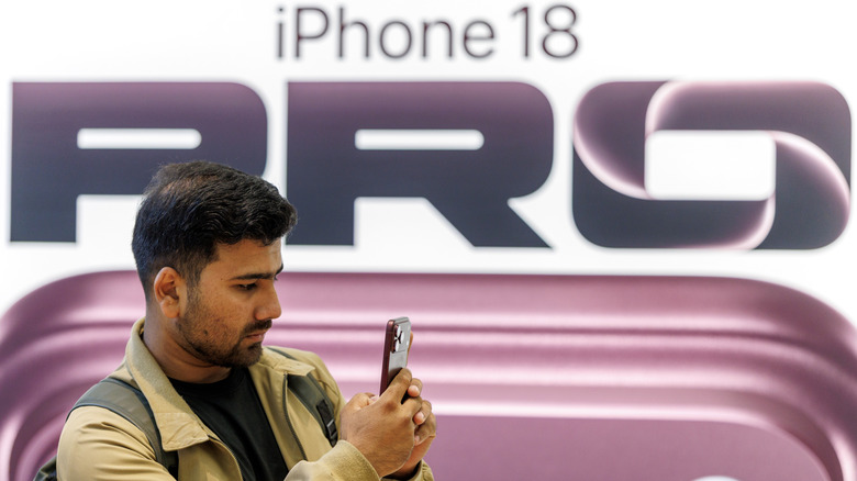 A person using an iPhone 18 Pro phone in front of an iPhone 18 Pro billboard.