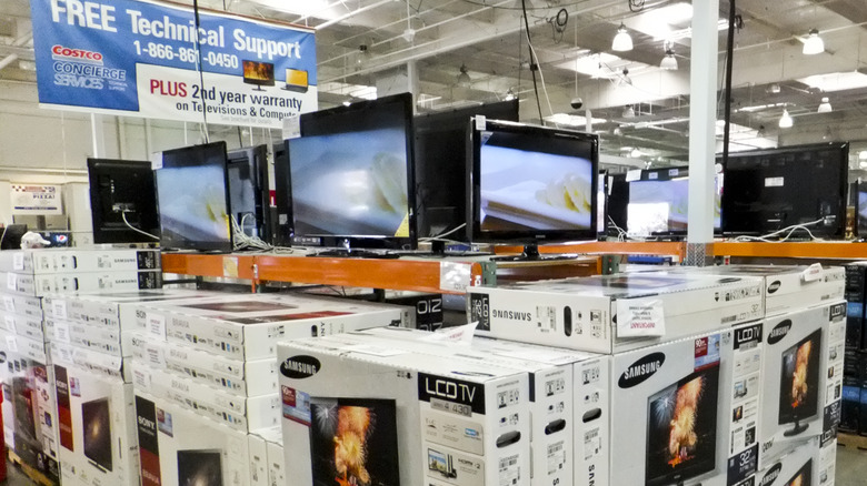 A stack of Samsung TVs in a Costco with a tech support banner in the background.