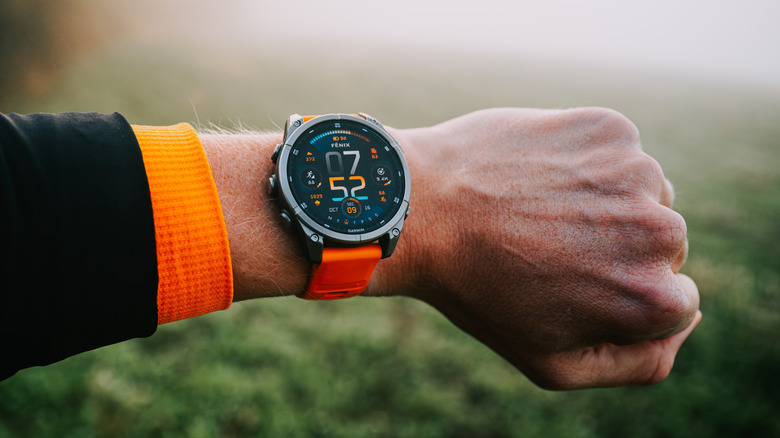 Close-up of a wrist wearing a Garmin smartwatch with terrain in the background