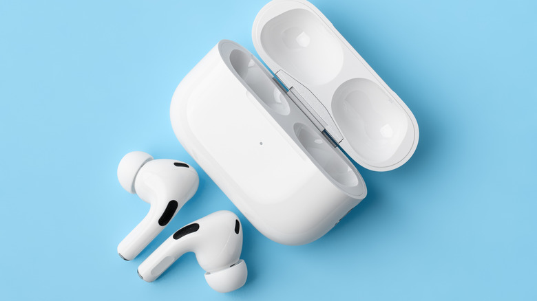 White Apple AirPods Pro sitting outside of their charging case against a blue backdrop