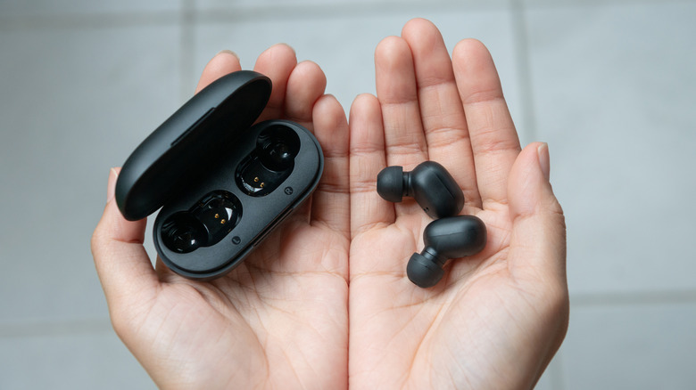 Two hands close together, one hand holds two black earbuds, whereas the left holds a black earbud charging case