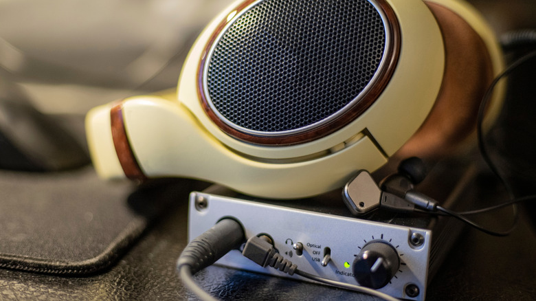 A pair of cream-colored headphones with wooden trim rest upon a small digital-to-analog (DAC) device