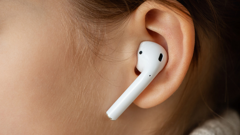 A closeup of a white Apple AirPod sitting snguly in an individual's right ear