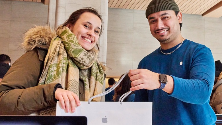 A customer and an Apple Retail representative holding an Apple shopping bag