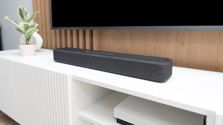Soundbar placed below a TV on a modern media console with a plant nearby.
