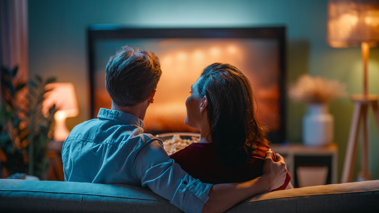 Couple sitting on a couch watching TV together in a living room.