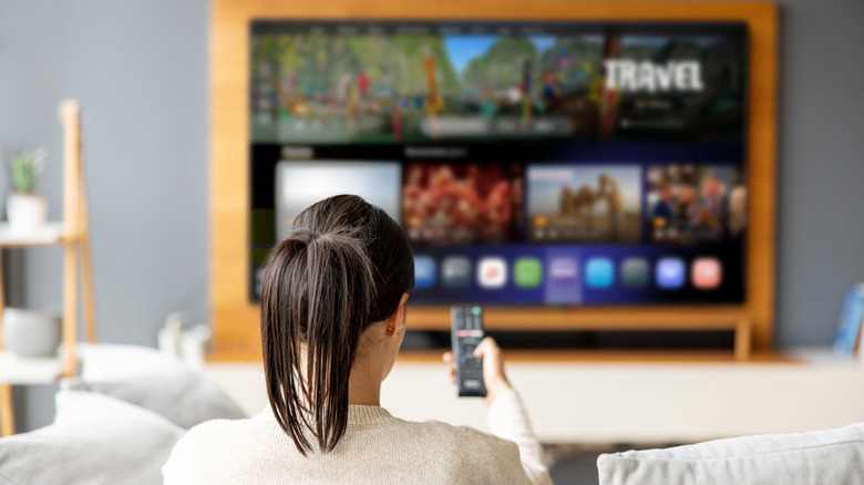 Person using a remote control to navigate a smart TV interface from a couch.
