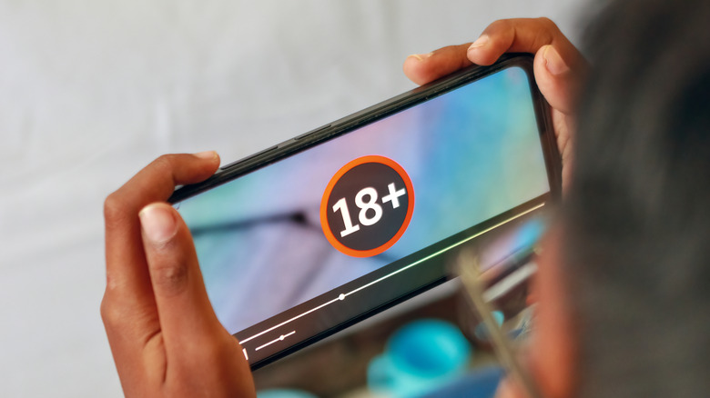 A child holding a phone showing an 18+ content rating