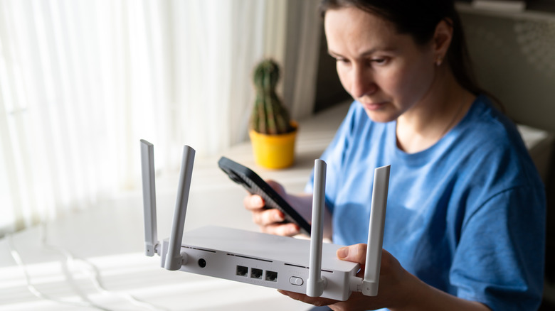 A woman holding a router in one hand with a phone in the other