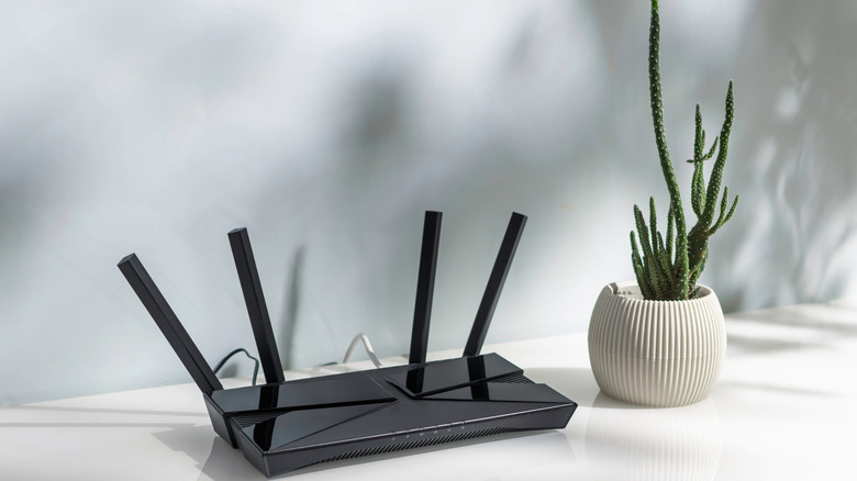 A black router with multiple antennas sitting on a table top next to a plant