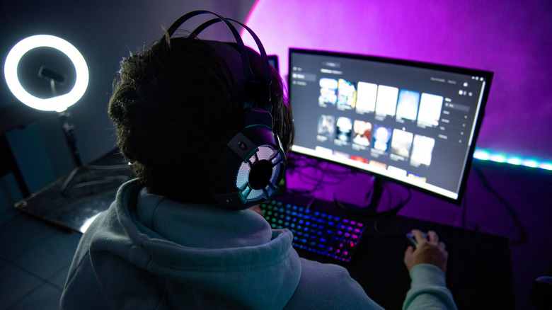 Person wearing RGB gaming headset using a PC with illuminated keyboard and monitor.