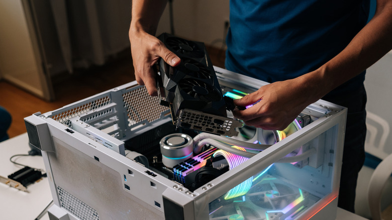 Person installing a GPU into a desktop PC with RGB components inside the case.