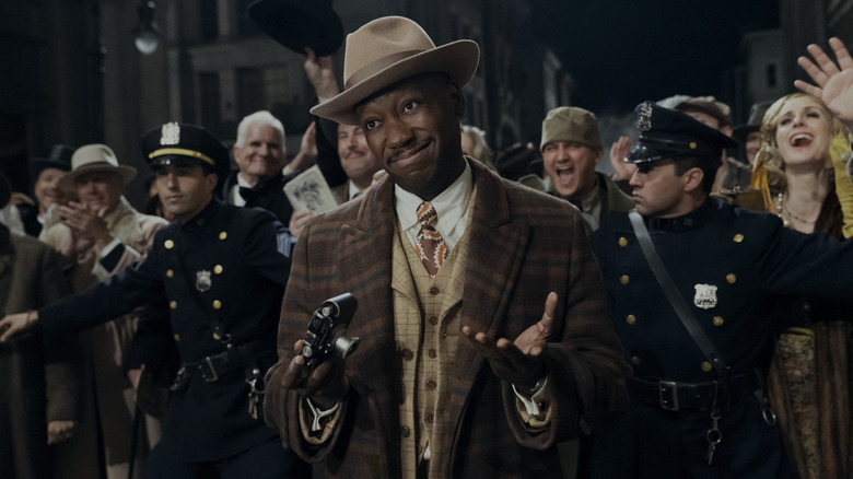 Lamorne Morris as Robbie Robertson holding a camera with a crowd behind him in Spider-Noir