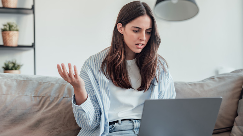 Woman sitting on a couch acting frustrated as her laptop is running slow