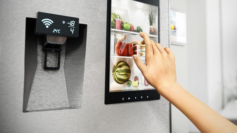 Person using a touchscreen on a smart refrigerator with a water dispenser display beside it.