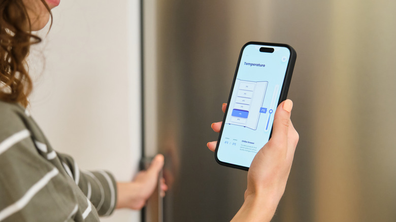 Person using a smartphone app to adjust the temperature of a smart refrigerator.