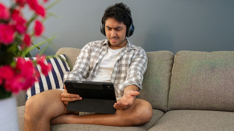 Person wearing headphones looking annoyed at their tablet