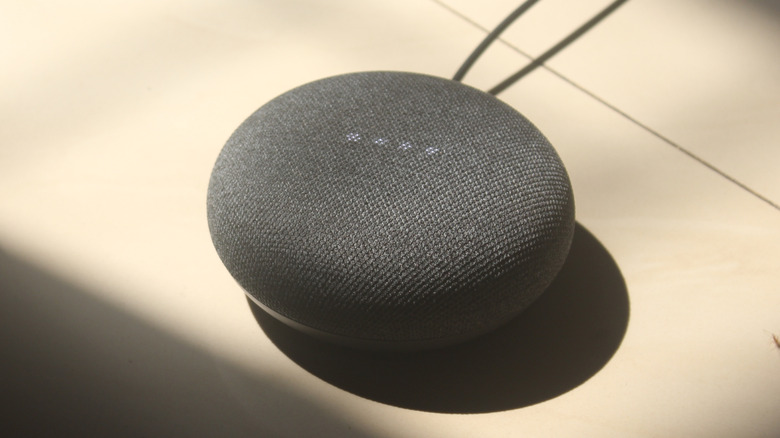 A Google Home Mini (Charcoal Black) sitting by itself on a slightly shaded surface.