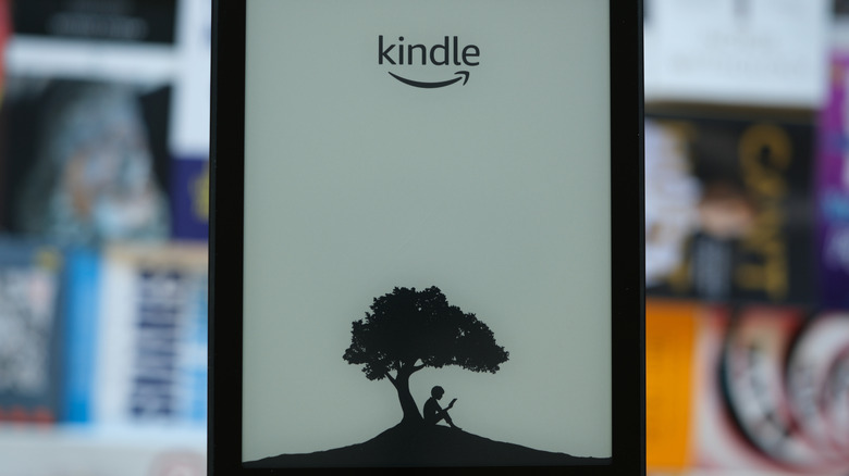Close-up of an Amazon Kindle with books out of focus in the background