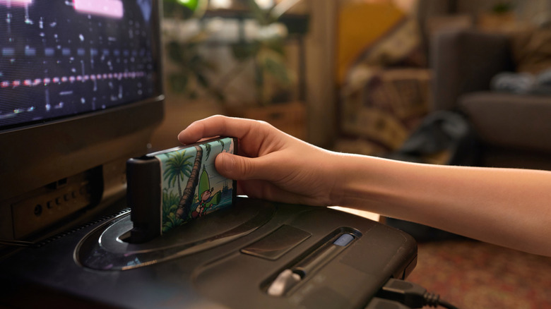 A person inserting a retro cartridge into a gaming console in front of a CRT