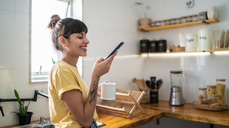 Young woman using the mobile phone while drinking coffee or tea at home