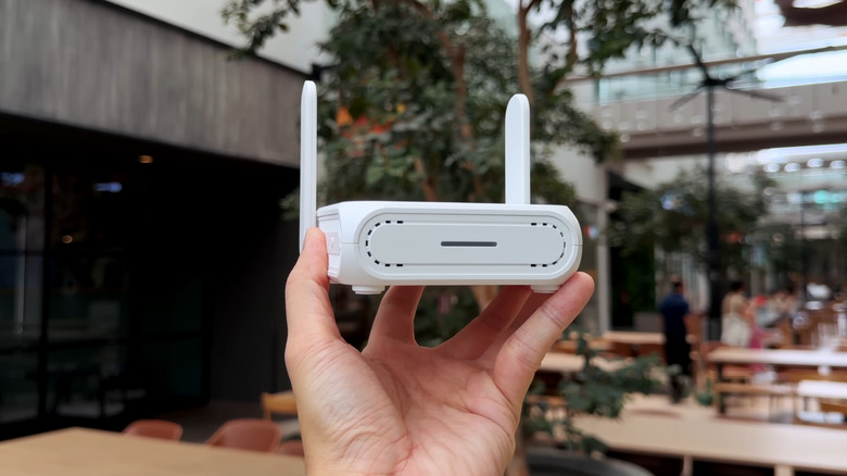 person holding a white ASUS travel router in a cafe