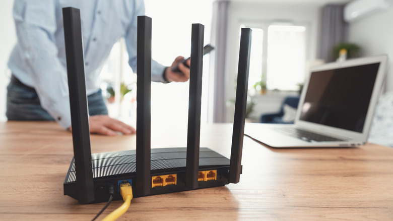 router placed on a wooden table alongside a laptop with a person standing in the background