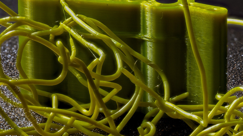 Brittle filament littering a failed 3D print project still attached to the print bed.