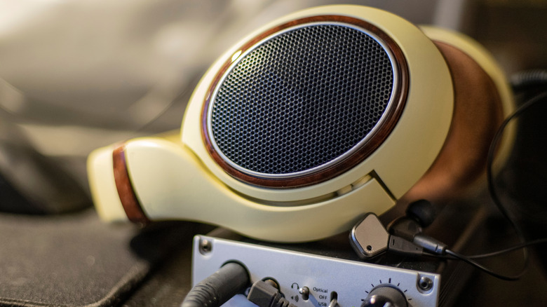 A pair of cream-colored headphones with wooden trim sit atop a small DAC