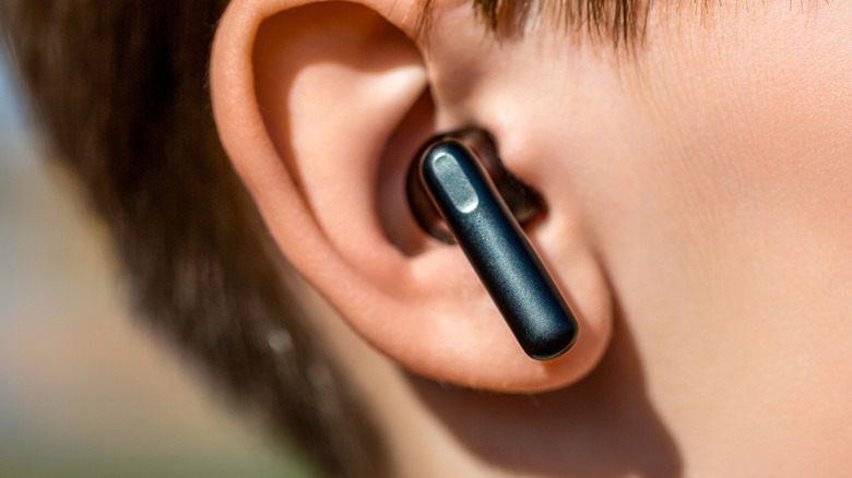 A closeup of a black earbud nestled in a user's right ear