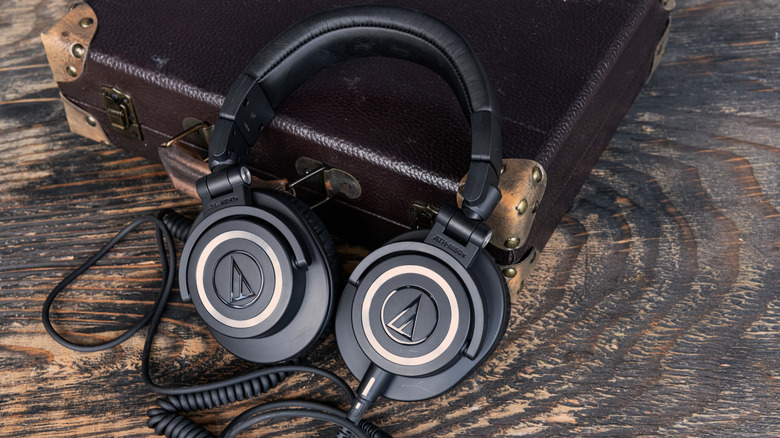 A pair of black Audio Technica headphones sit on a wooden surface while also resting against a brown leather briefcase