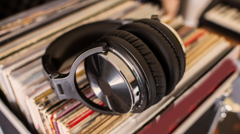A pairof silver and black headphones sitting on top of a pile of assorted records