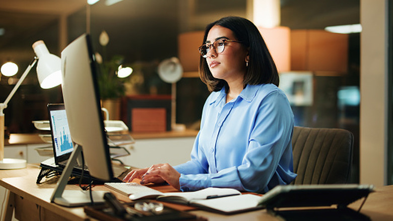 A woman working at a desk, using a computer in a home office.