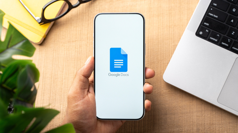 A hand holding a phone with the Google Docs logo on it