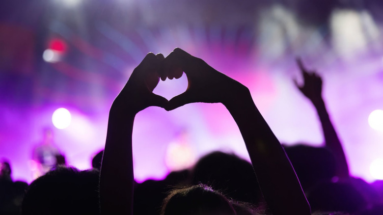 Picture of a concert, where a person in the audience is making hearts with their hands