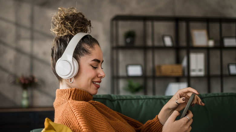 A woman smiling and listening to music with headphones on as she looks at her phone