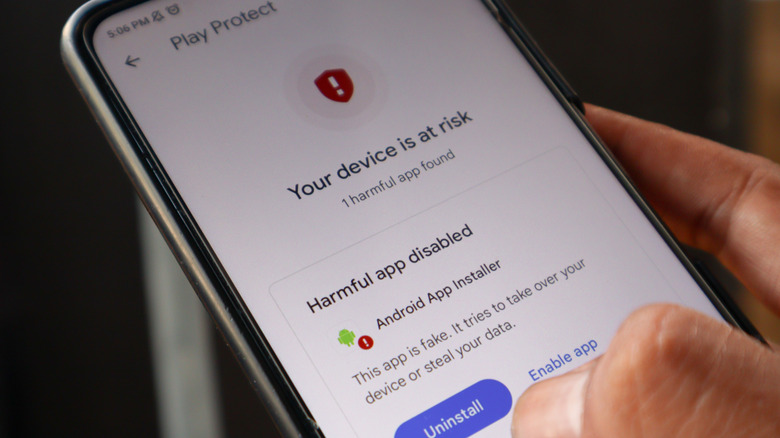 person holding a smartphone showing the google play protect malicious app warning