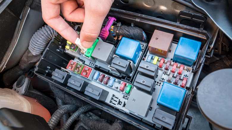 A hand taking out a fuse in the fuse box of a car.
