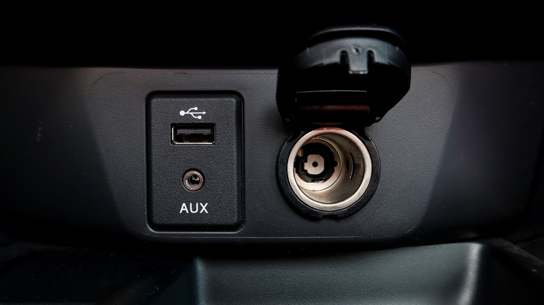 Close-up of a car's USB port, AUX port, and cigarette lighter adapter.