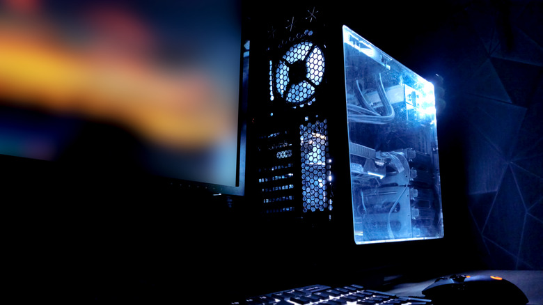 Gaming PC with blue internal lighting beside a monitor, keyboard, and mouse.