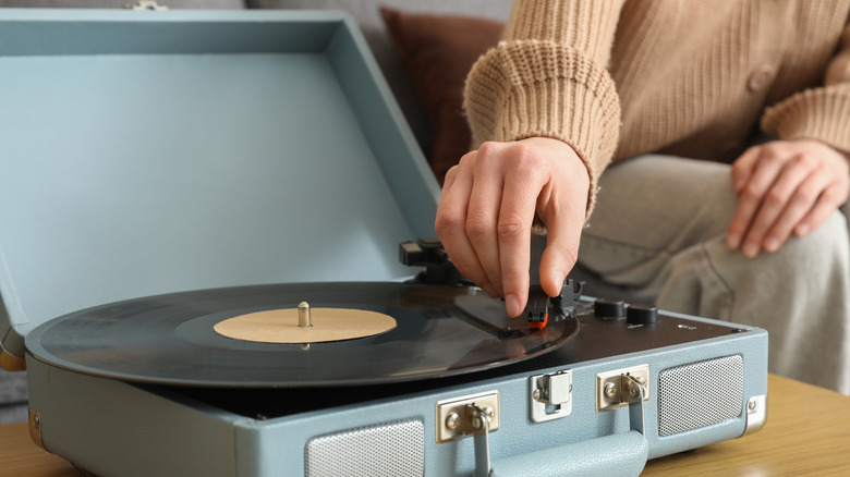 Close up of a hand reaching for the cartridge of a record player. The player is light blue and resembles an open suitcase.